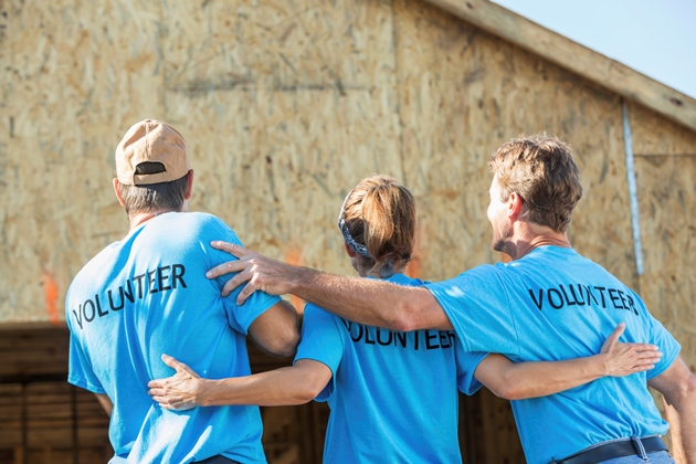 Rear view of group of volunteers helping to build a house for a family in need, standing in front of home under construction.